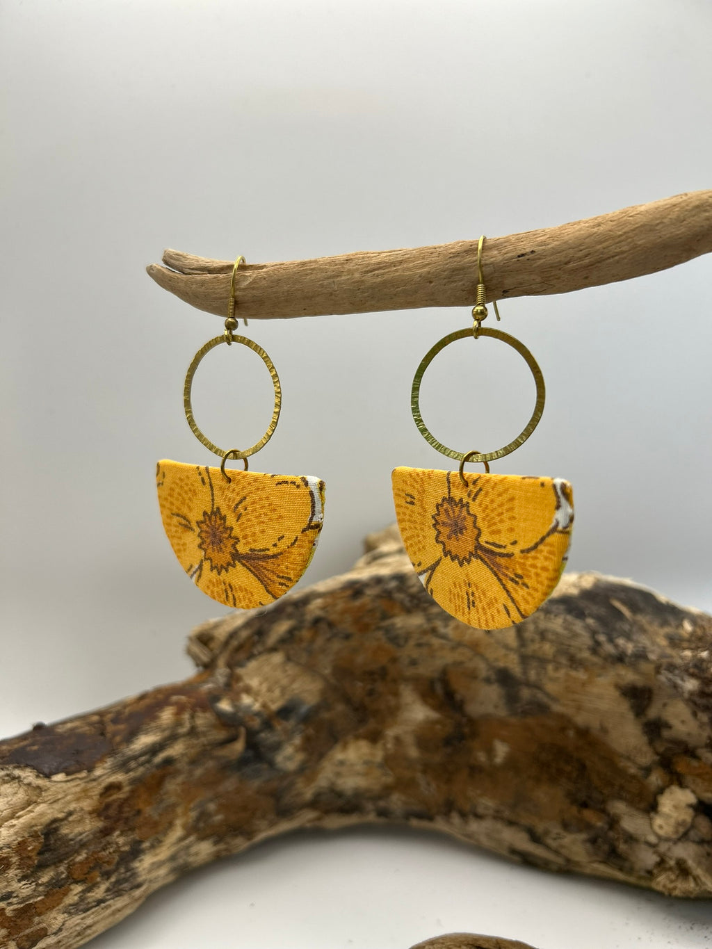 orange floral earrings hanging from a branch on a neutral background