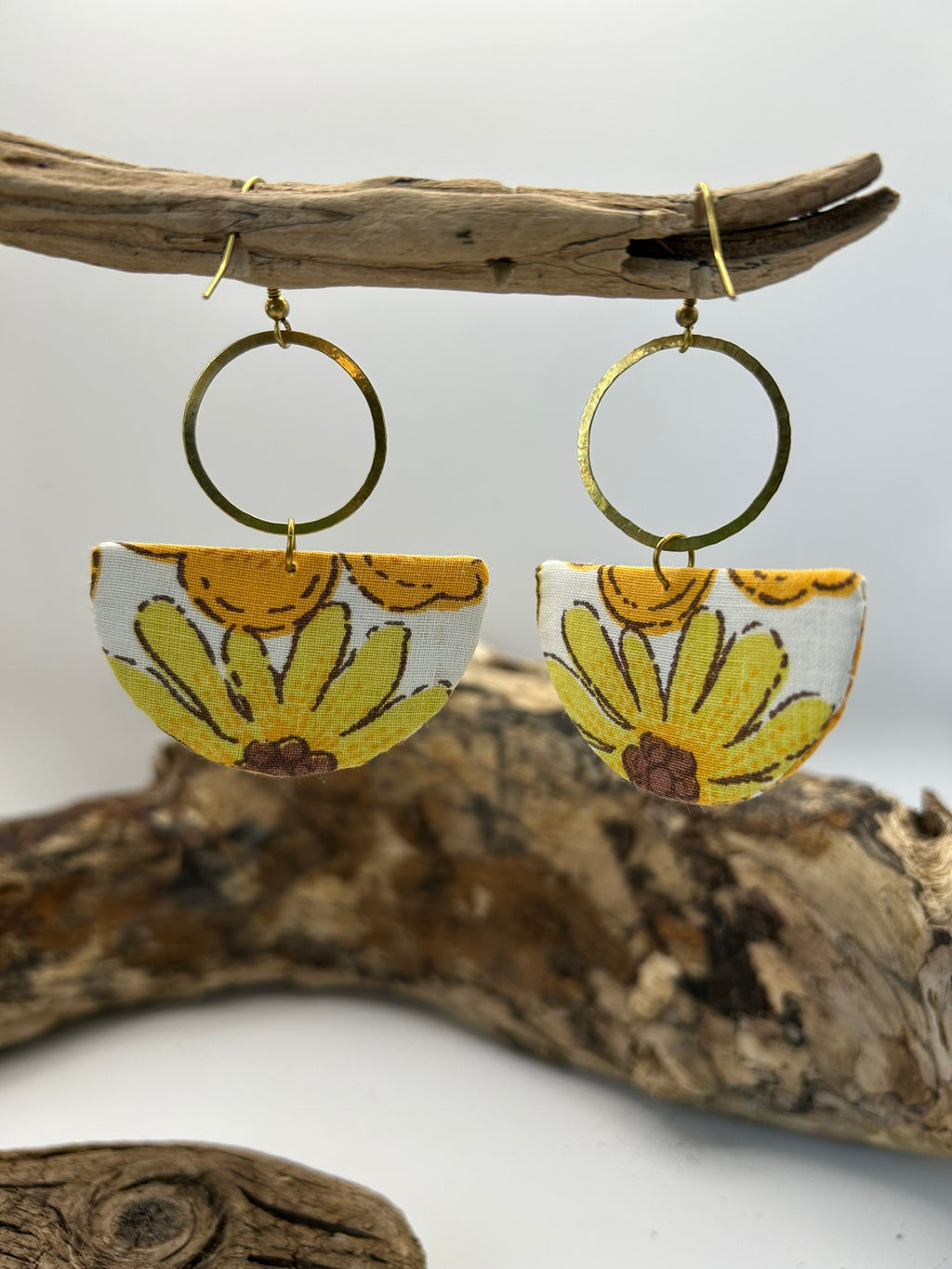 Pair of earrings with floral design hanging on a branch against a white background