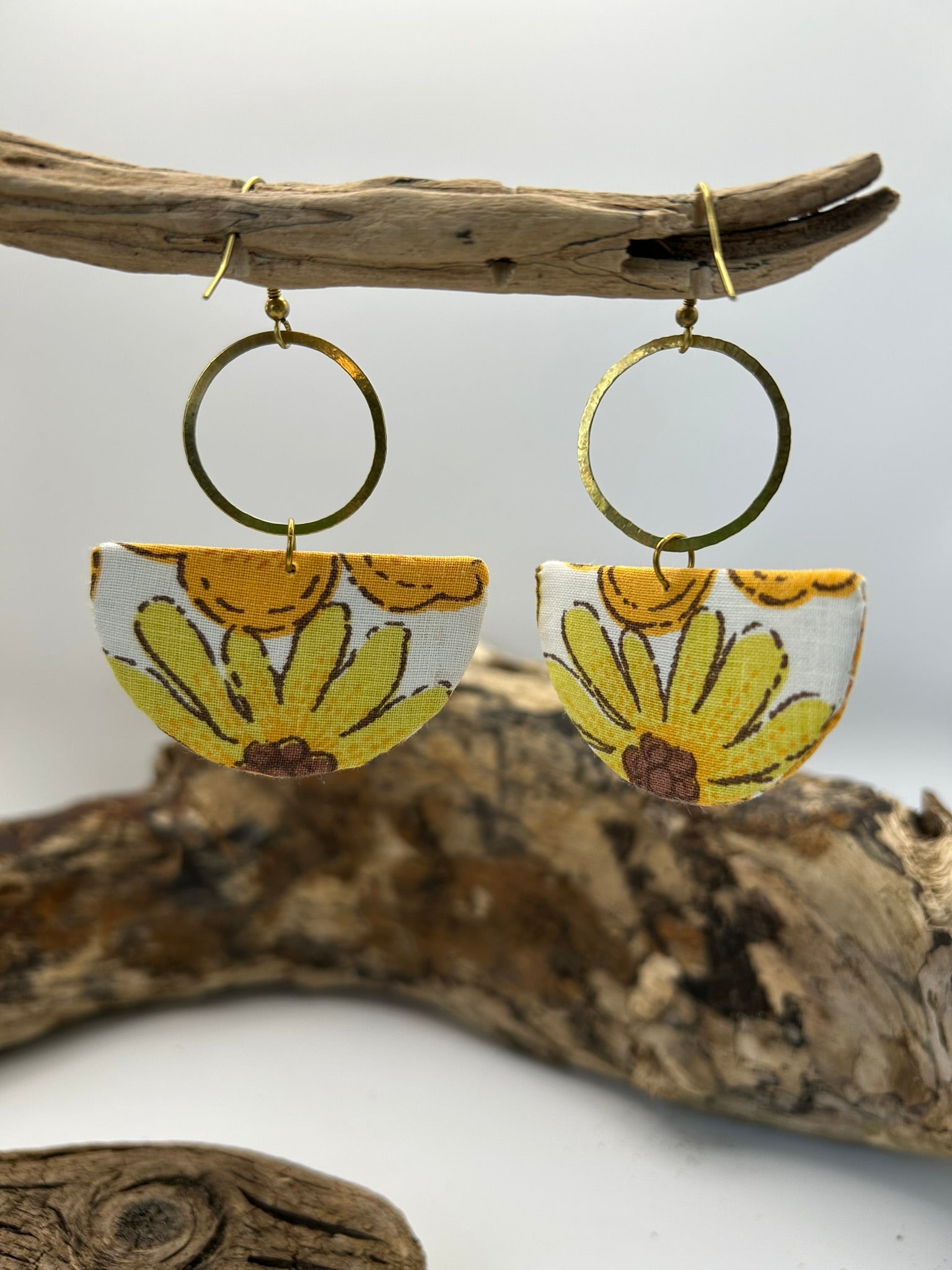 Pair of earrings with floral design hanging on a branch against a white background