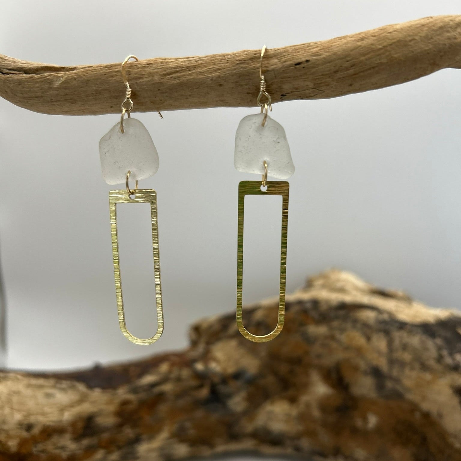 Joy Sea Glass earrings with brass D shape attachment.  
A pair of earrings made from clear sea glass and brass attachment.  Displayed on driftwood with a white backdrop.