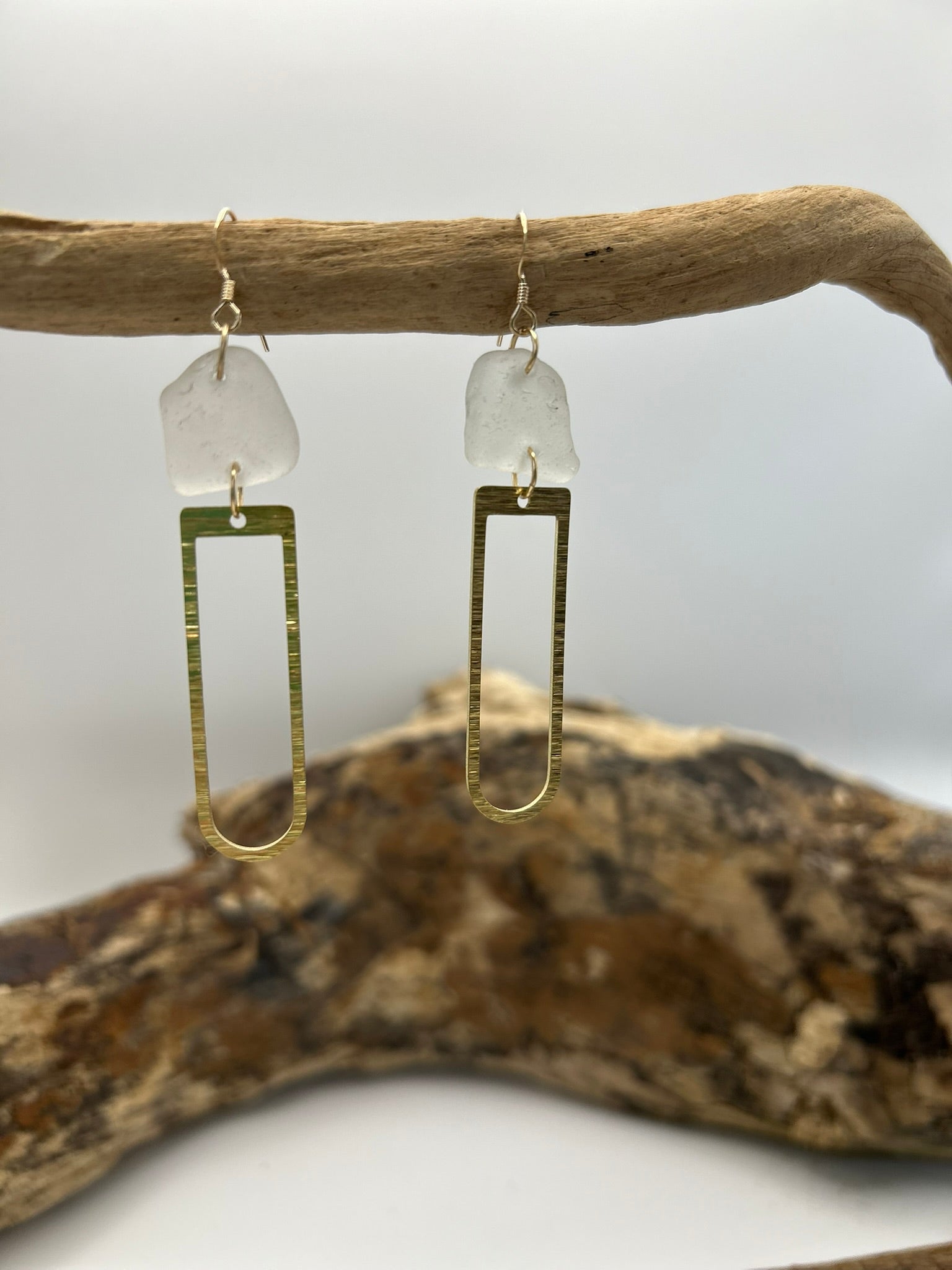 Joy Sea Glass earrings with brass D shape attachment.  
A pair of earrings made from clear sea glass and brass attachment.  Displayed on driftwood with a white backdrop.