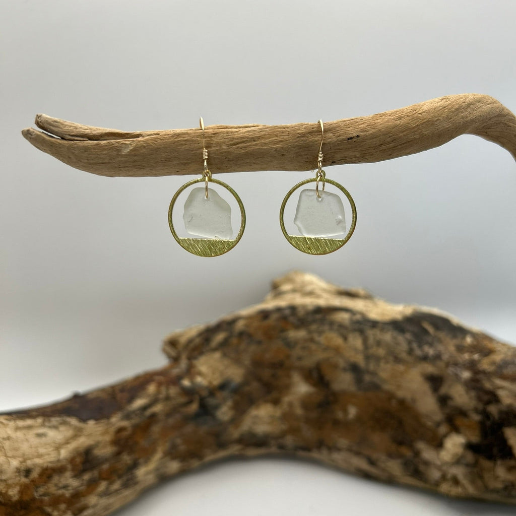 Joy Sea glass earrings - mini clear circles. 
Pair of earrings with clear sea glass and brass surround displayed on a piece of driftwood against a white background
