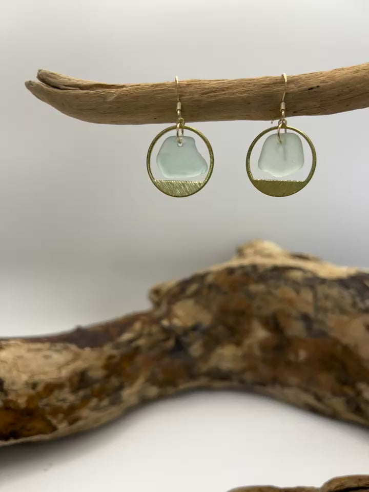 Joy Sea glass earrings - mini clear circles. 
Pair of earrings with clear sea glass and brass surround displayed on a piece of driftwood against a white background