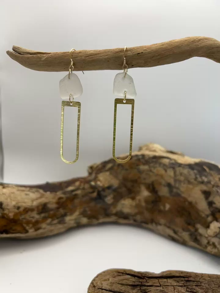 Joy Sea Glass earrings with brass D shape attachment.  
A pair of earrings made from clear sea glass and brass attachment.  Displayed on driftwood with a white backdrop.