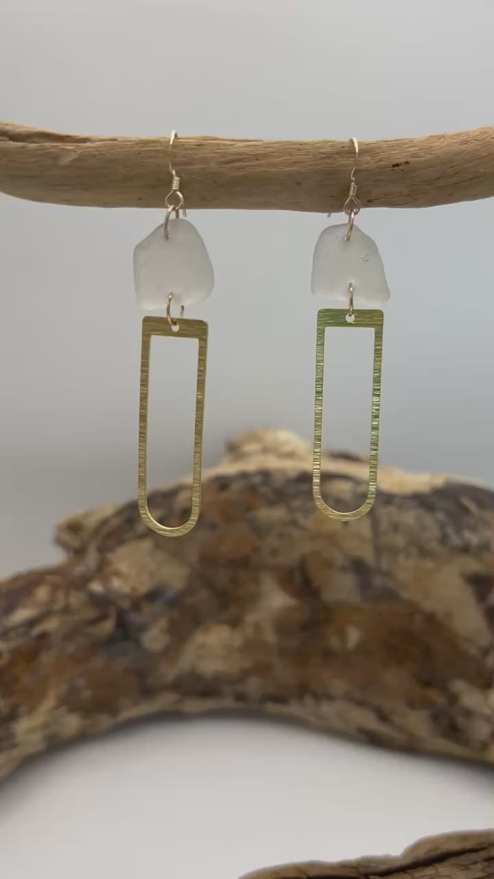 Joy Sea Glass earrings with brass D shape attachment.  
A pair of earrings made from clear sea glass and brass attachment.  Displayed on driftwood with a white backdrop.